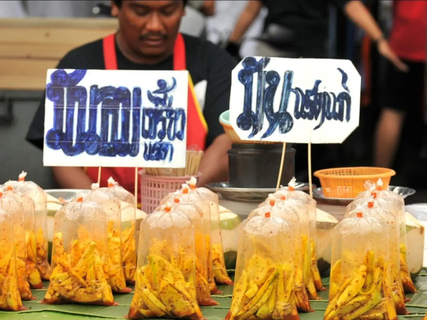 Sprzedawca na targu Chatuchak z porcjami tajskich przekąsek zapakowanych w plastikowe torebki