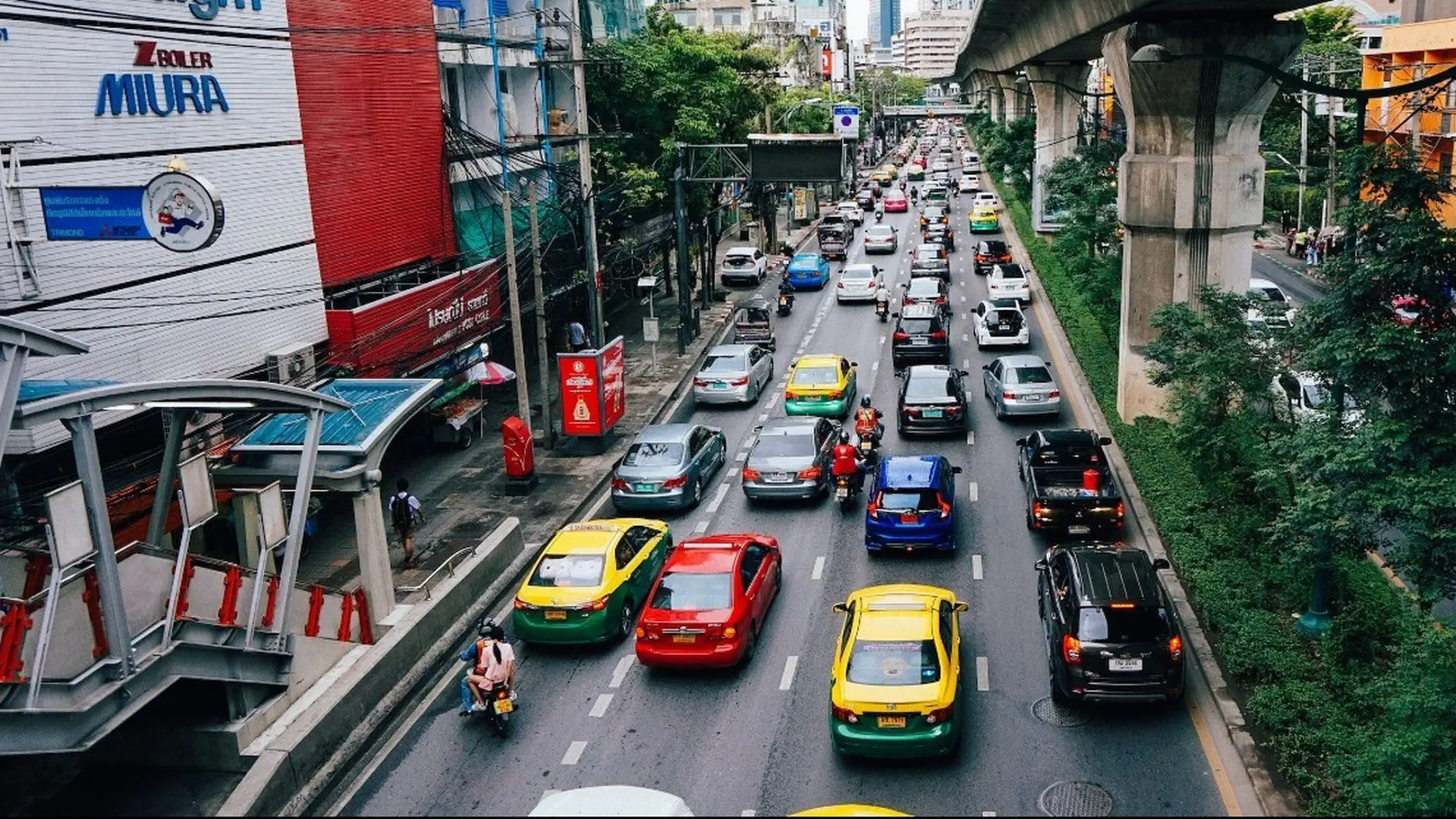 Kolorowe taksówki i ruch uliczny w centrum Bangkoku, z widocznym torowiskiem BTS Skytrain
